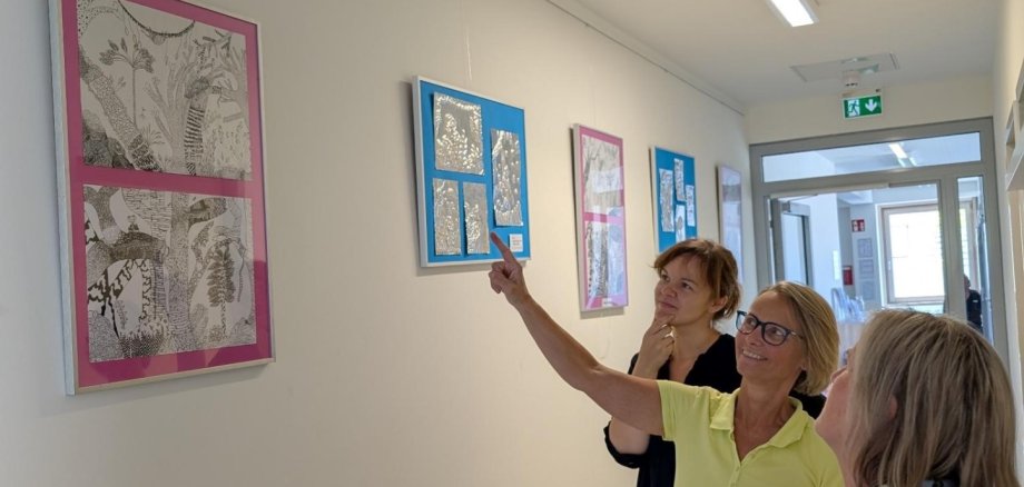 ثلاث نساء ينظرن إلى صور مؤطرة معلقة على جدار أبيض في ردهة أحد المراكز العائلية ويشيرن إليها