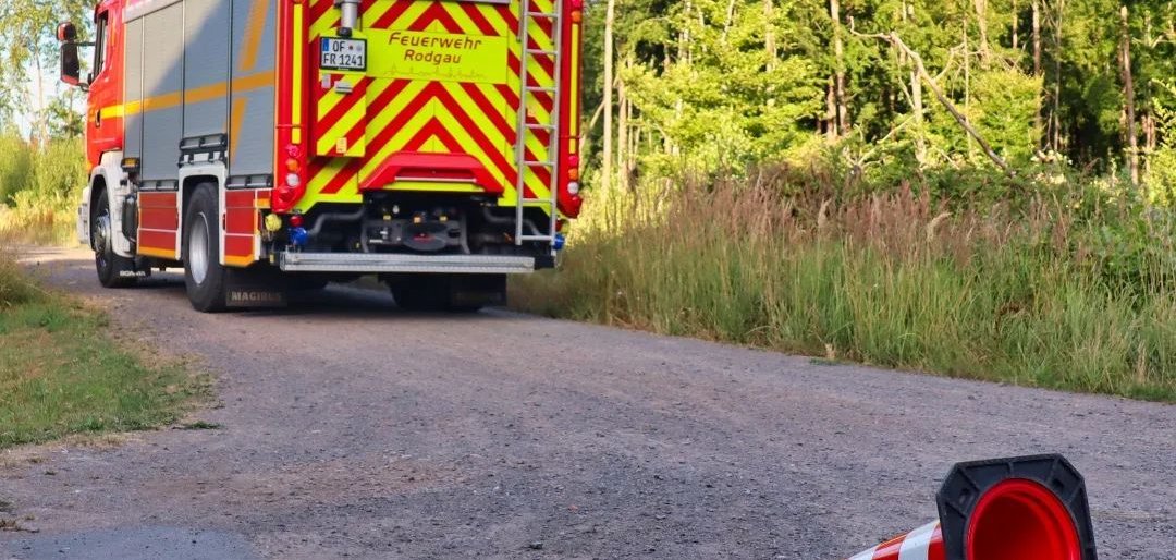 سيارة إطفاء تحمل علامات تحذيرية على طريق غابي بجانب مخروط مرور مقلوب