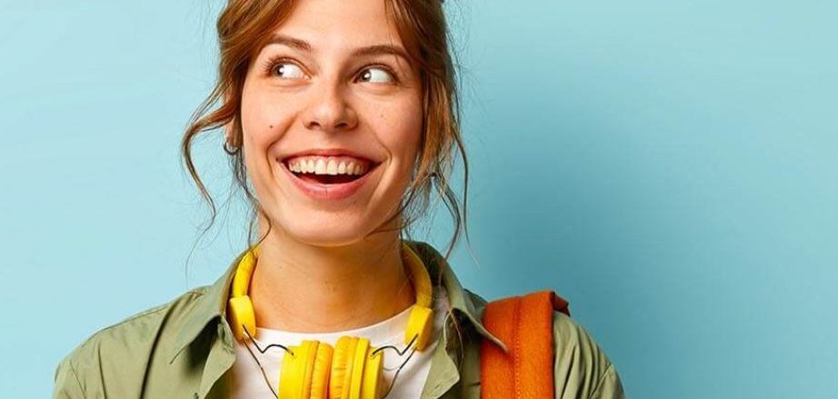 شخص شاب يرتدي سماعات صفراء حول عنقه وسترة خضراء وحقيبة ظهر برتقالية اللون تشير إلى اليسار