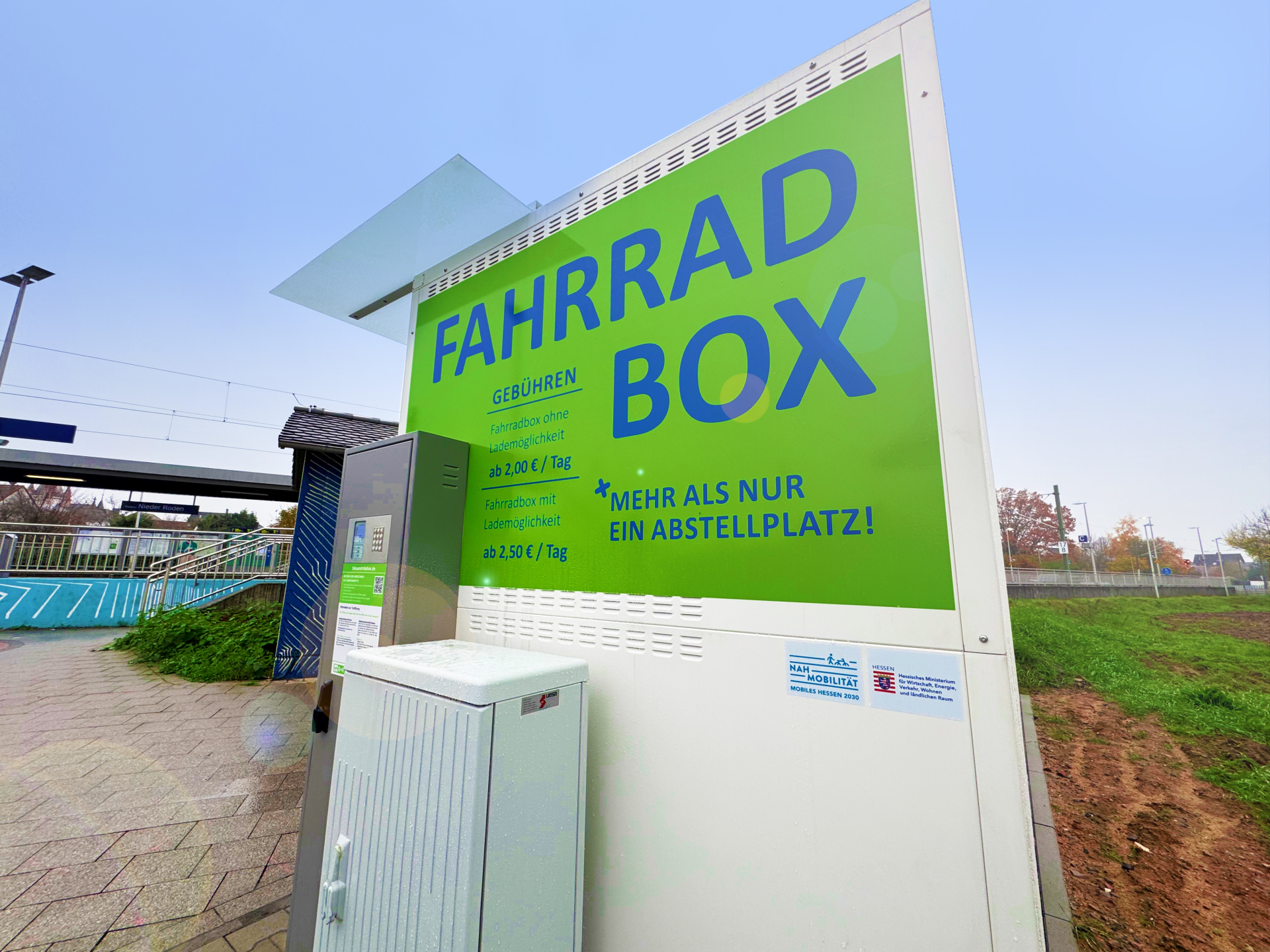 Зелена табела с надпис "FAHRRAD BOX" и информация за цените на кутиите за велосипеди на железопътната гара в Нидер-Роден.
