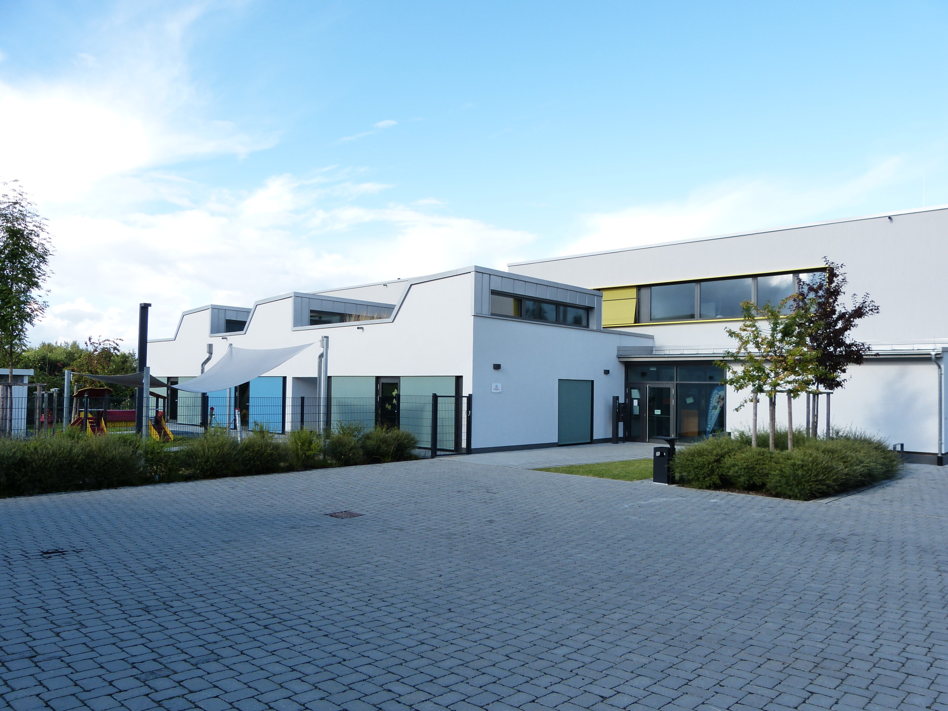 Modern, white building of the family centre with a paved forecourt, several windows and a small tree in front of it.