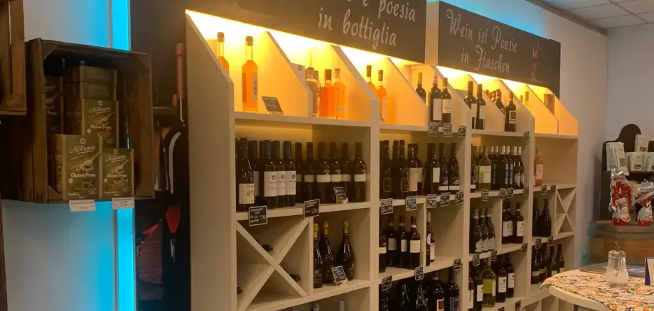 Shelf with various bottles of wine and spirits, above two signs with the texts 'Wine is poetry in bottles' and 'Wine is poetry in bottiglia'.