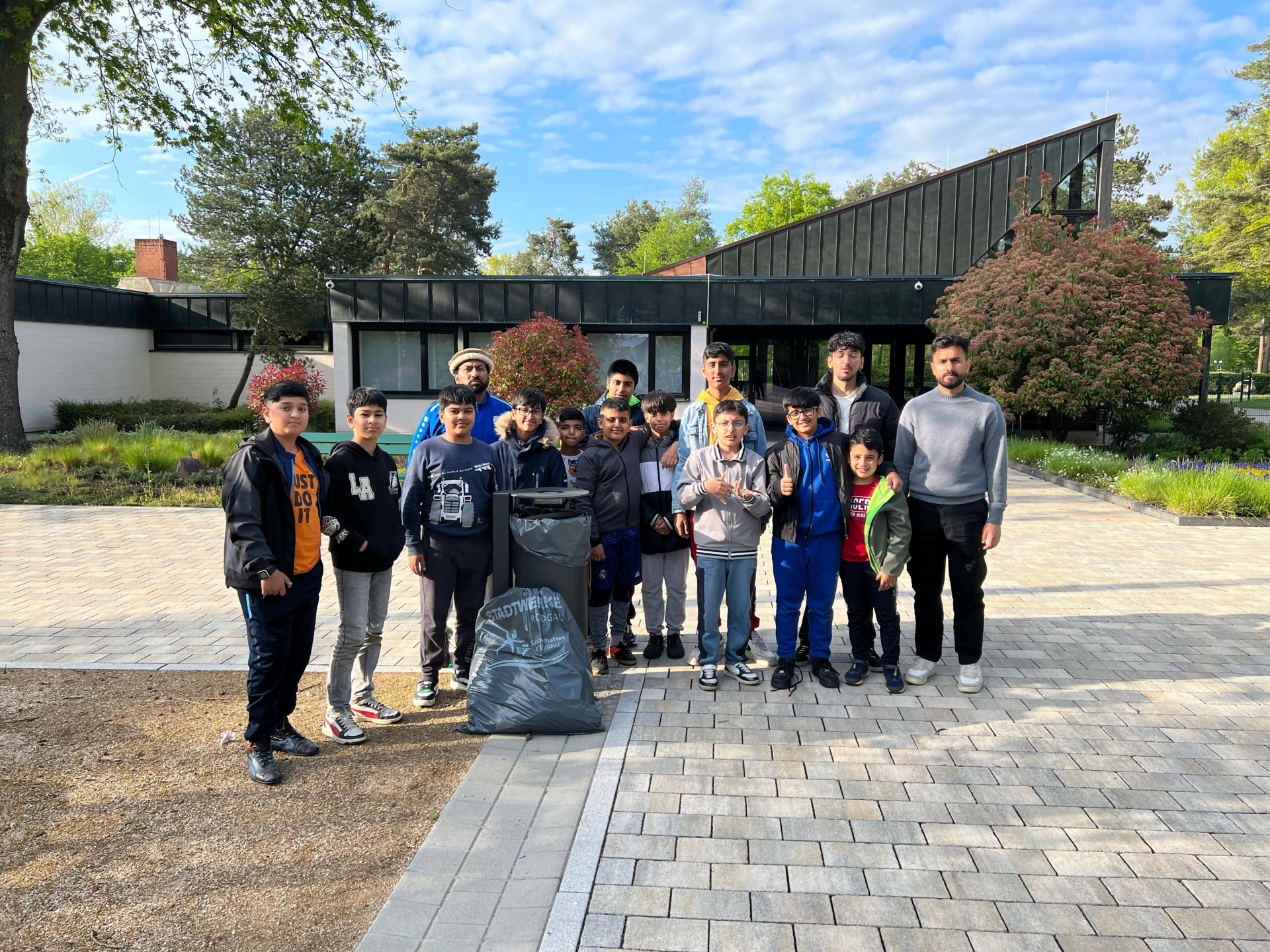 Public utilities clean Rodgau Group of twelve people standing in front of a modern building. Some are holding a large rubbish bag. Trees and bushes are visible in the background.