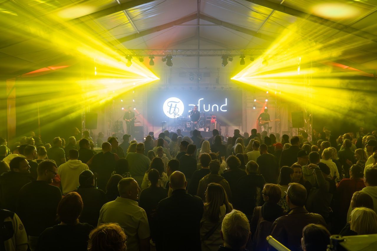 Rodgau Open Industry Festival A crowd stands in a tent and watches a band playing on a stage. Yellow beams of light shine from the ceiling onto the audience.