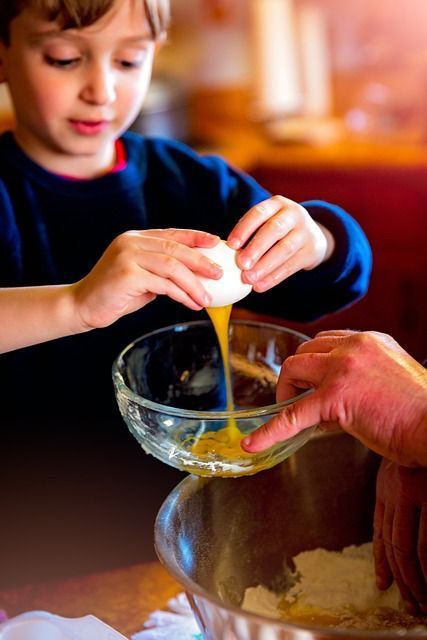 Healthy cooking A child breaks an egg and puts the yolk and white into a glass bowl.