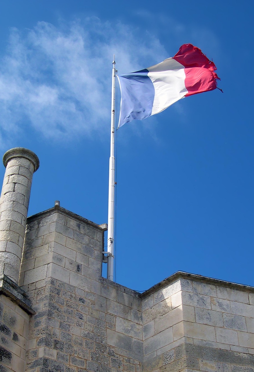 vhs French French flag in the colours blue, white and red, flies on a high mast on a historic building with stone walls.