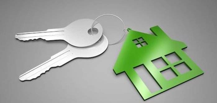 Two silver keys with a key ring on which hangs a green house symbol with windows.