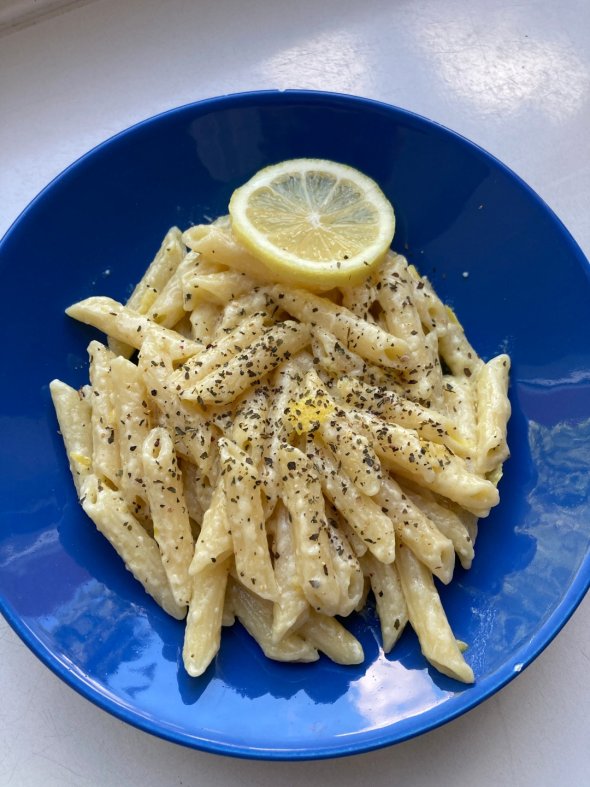 Plate of penne in a creamy sauce, garnished with black pepper and a slice of lemon on a blue plate.