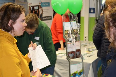 Visitors at an exhibition stand with information material and green balloons at an education fair