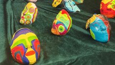 Colourful, hand-painted masks with abstract patterns on green fabric, exhibited at Jugend Art