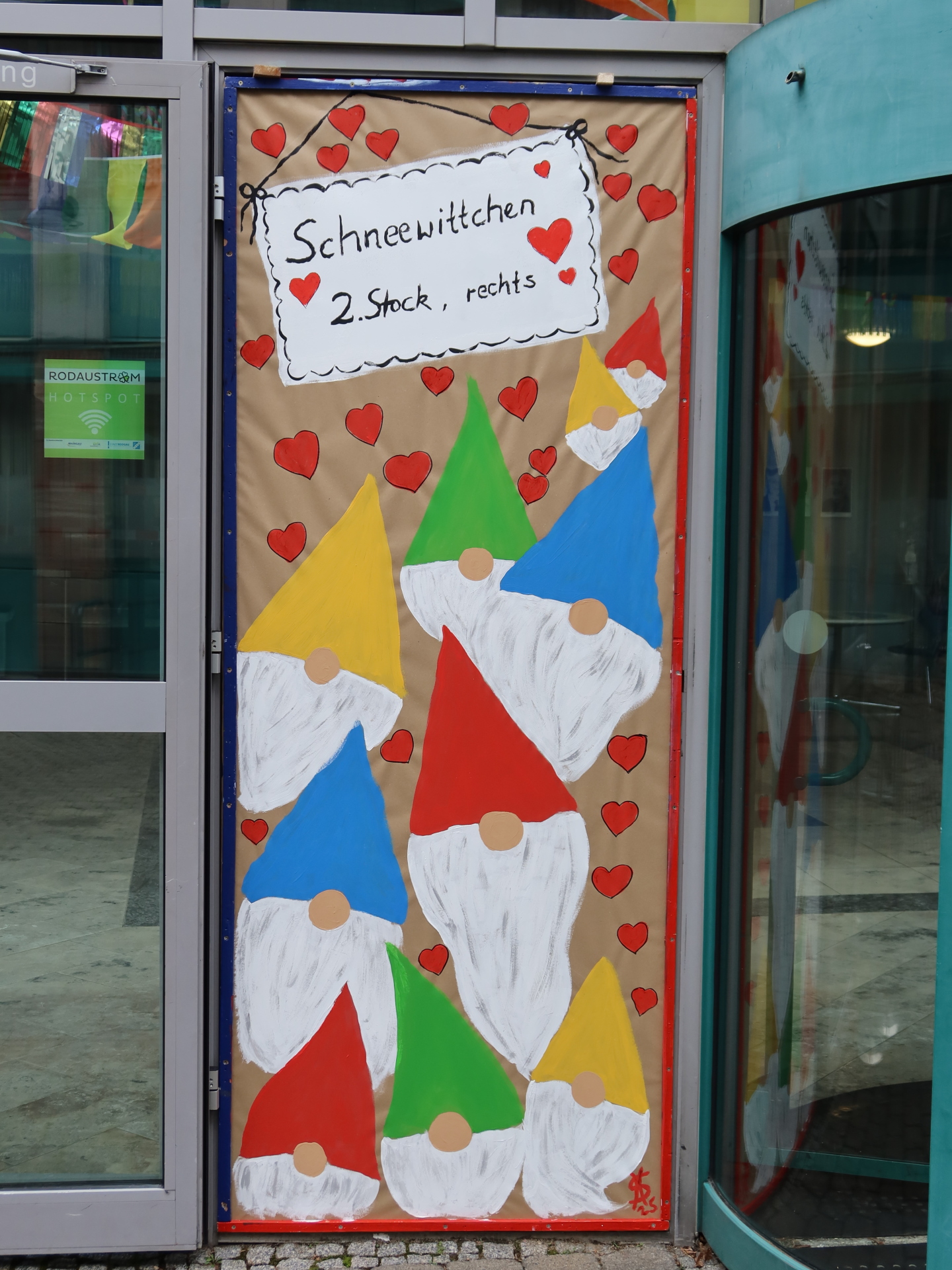 Colourful door decoration of the town hall door with several dwarfs in red, yellow and blue standing on a brown background. At the top it says 'Snow White 2nd floor, right'.
