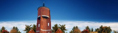 The top of the water tower can be seen against a blue sky and tree tops at the bottom of the picture.