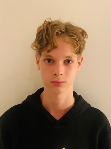 David Scales A young man with curly, blond hair and a black hooded jumper against a light-coloured background