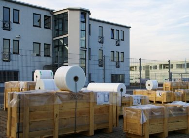 Industrial estate with several large wooden crates and white castors on a paved courtyard in front of a modern office building