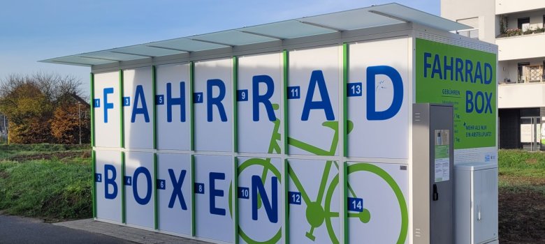 White bicycle box with blue lettering 'FAHRRAD BOXEN' and green bicycle pictogram at Nieder-Roden railway station.