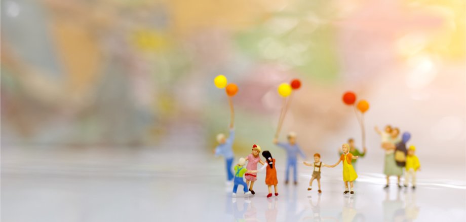 Imagen simbólica de la época de la convivencia Grupo de figuritas diminutas con globos de colores sobre un fondo claro, delante de un fondo difuminado y de colores