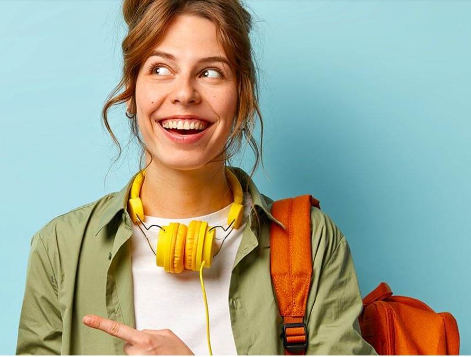 Joven con auriculares amarillos alrededor del cuello, chaqueta verde y mochila naranja apuntando a la izquierda