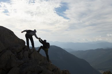 Dos personas escalando una montaña Una persona ayuda a otra a escalar una roca en la montaña