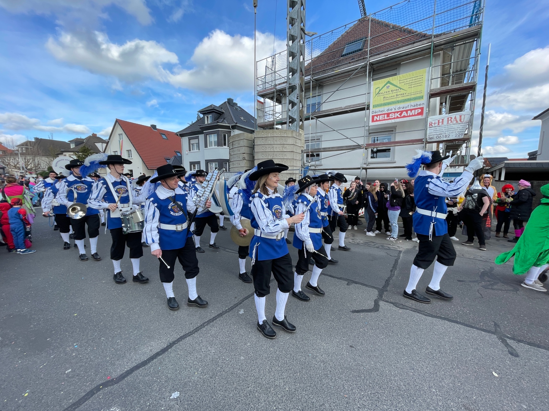 La banda de Obernau en traje azul y blanco con sombreros negros y medias blancas en el desfile de carnaval de 2024, desfilando por la calle ante los espectadores.