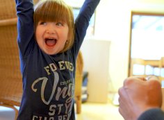 Un niño riendo levanta las manos en el aire - una guardería al fondo