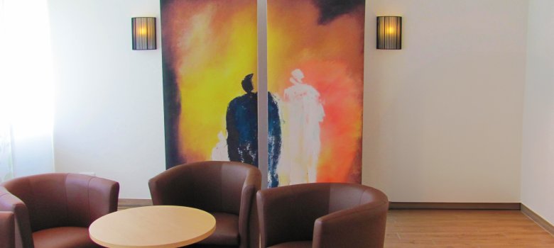 Habitación de despedida con zona de estar En primer plano hay tres asientos individuales de cuero y al fondo un cuadro con dos figuras abstractas en blanco y negro.