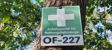 Panneau vert orné d'une croix blanche et portant l'inscription « Point de rassemblement pour les véhicules de secours OF-227 », fixé à un arbre dans la forêt