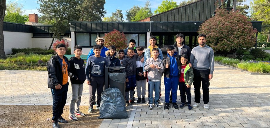 Groupe de douze personnes debout devant un bâtiment moderne. Certains tiennent un grand sac poubelle. Des arbres et des arbustes sont visibles à l'arrière-plan.