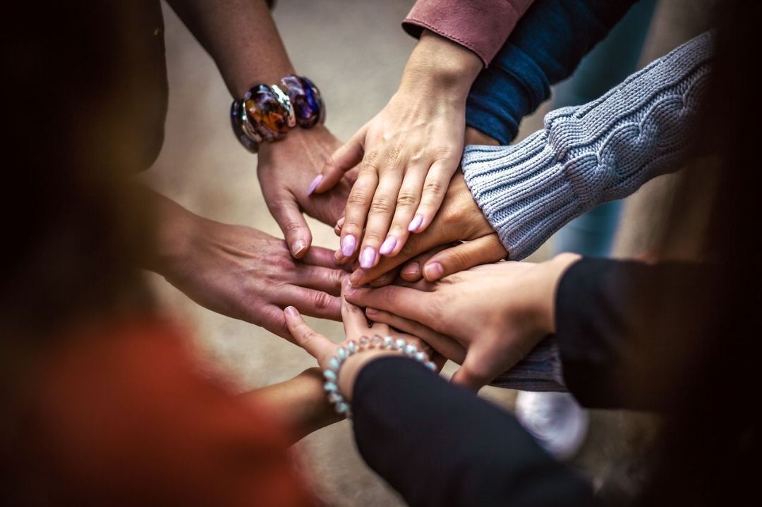 Différentes personnes debout en cercle tendent leurs bras et leurs mains vers le centre.