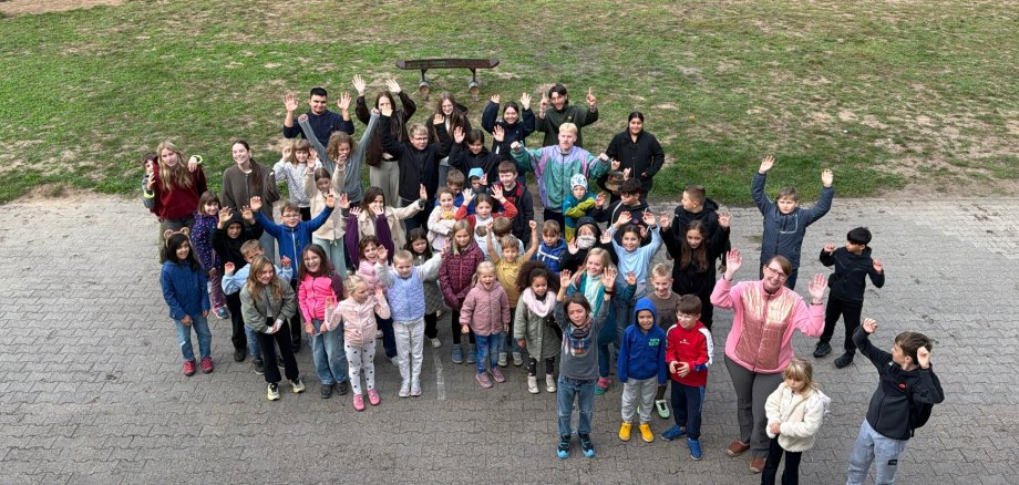 Ouverture des jeux de vacances d'automne Un groupe d'enfants et d'adultes se tient sur une place pavée et salue la caméra