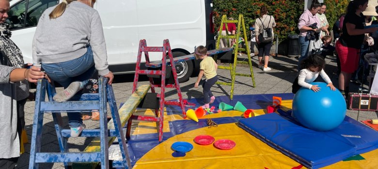 Les enfants jouent dans une aire de jeux colorée Des enfants jouent sur une aire de jeux colorée avec des échelles, des tapis et un gros ballon de gymnastique bleu lors d'une fête en plein air.