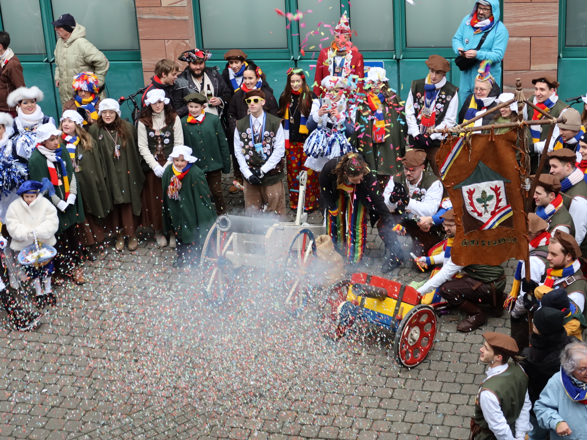 Groupe de personnes en costumes d'époque autour de deux petits canons tirant des confettis en l'air dans la cour de l'hôtel de ville