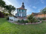 Rektor-Geißler-Haus avec jardin Rektor-Geißler-Haus à Dudenhofen, une maison historique à colombages avec des volets verts et blancs et une tour, entourée d'un jardin avec des fleurs et un banc blanc.