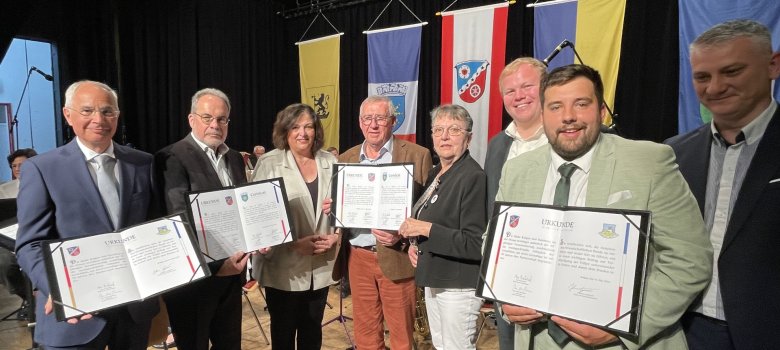Groupe de huit personnes sur scène lors de la célébration des jumelages, le troisième à partir de la droite est Max Breitenbach, plusieurs tiennent des certificats dans leurs mains.