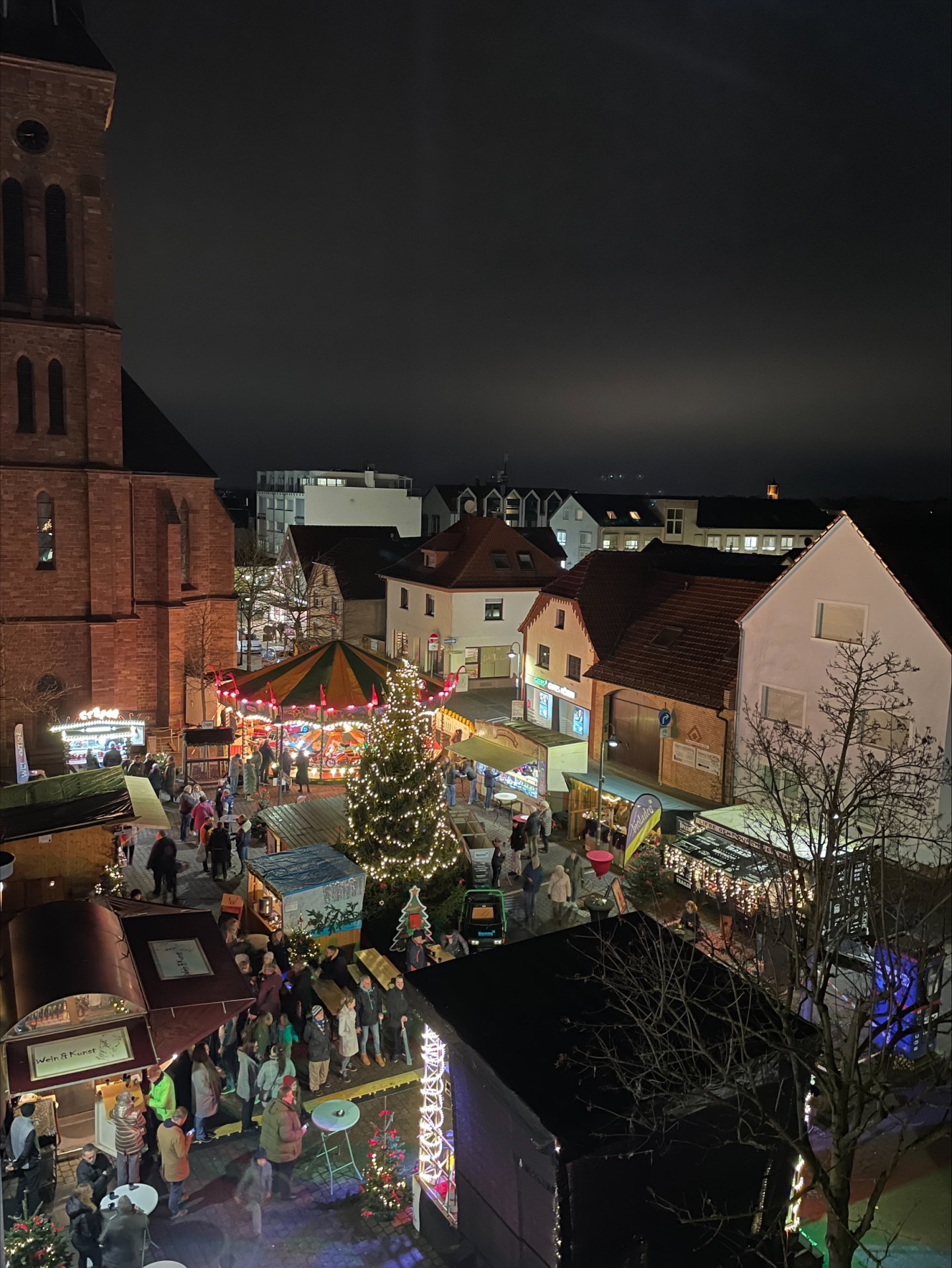 Marché de l'Avent en soirée sur la place de la mairie de Rodgau, avec un sapin de Noël illuminé, un manège et des stands de marché devant des bâtiments historiques.