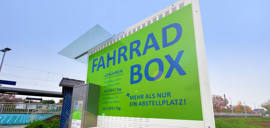Cartellone verde con la scritta "FAHRRAD BOX" e informazioni sui prezzi presso le cassette per biciclette della stazione ferroviaria di Nieder-Roden.