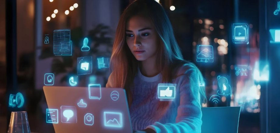 Persona seduta davanti a un computer portatile con icone fluttuanti e luminose di applicazioni digitali in un ambiente buio