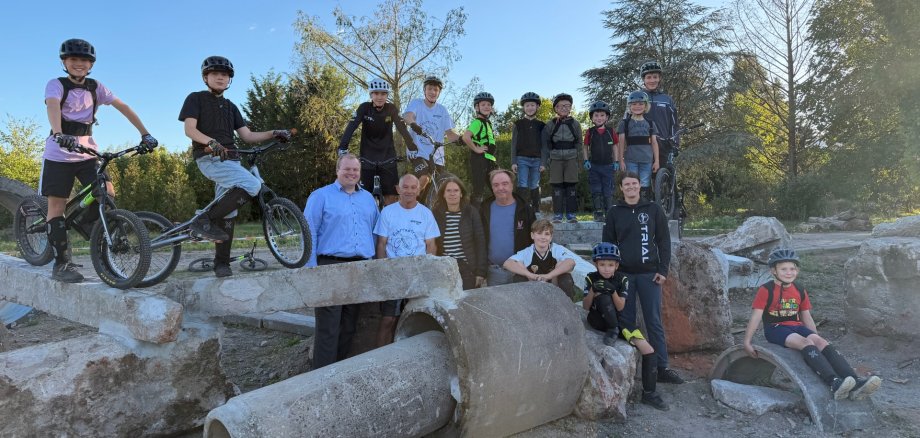 Nuova sede per la sezione trail del TSV Gruppo di bambini e adulti con caschi e biciclette su e intorno a grandi tubi di cemento e rocce all’aperto