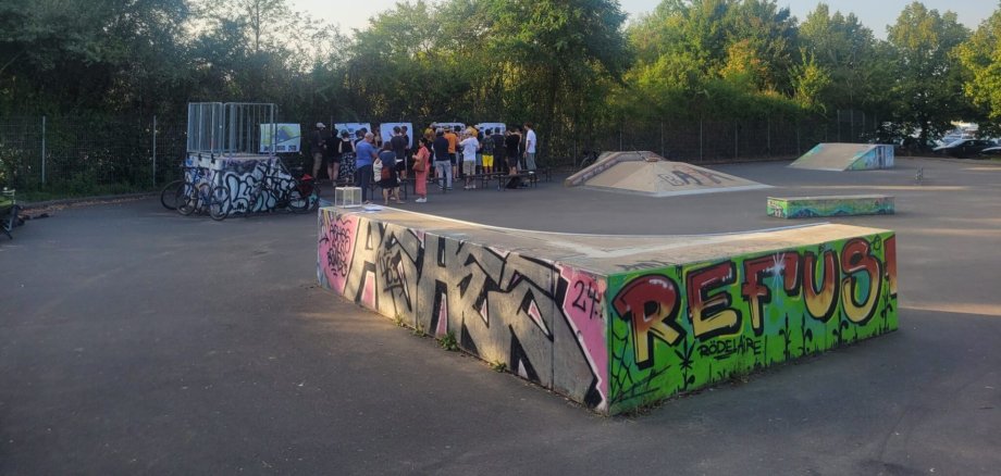Pista da skate presso lo stabilimento balneare con diverse rampe e un gruppo di persone sullo sfondo; una rampa è ricoperta di graffiti colorati