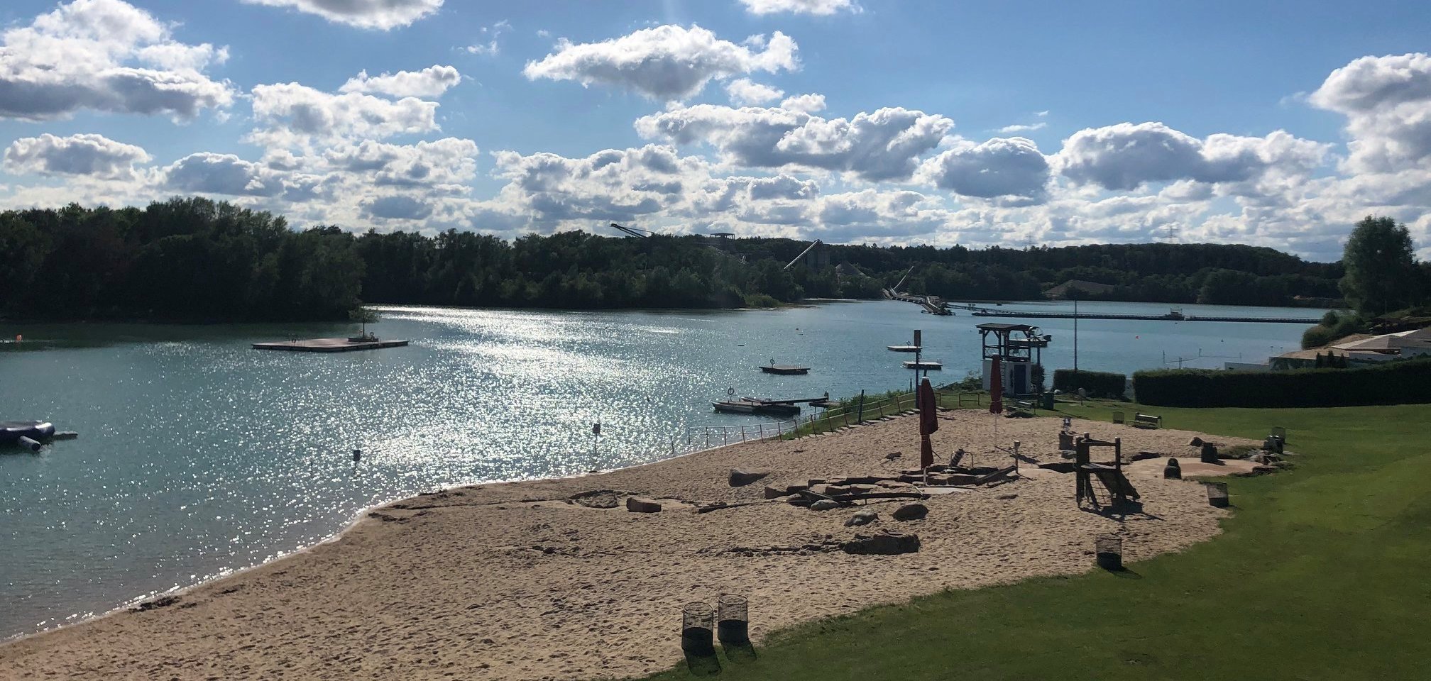 Una spiaggia con barche e un lago sullo sfondo, circondata da dolci onde e da una riva verde.