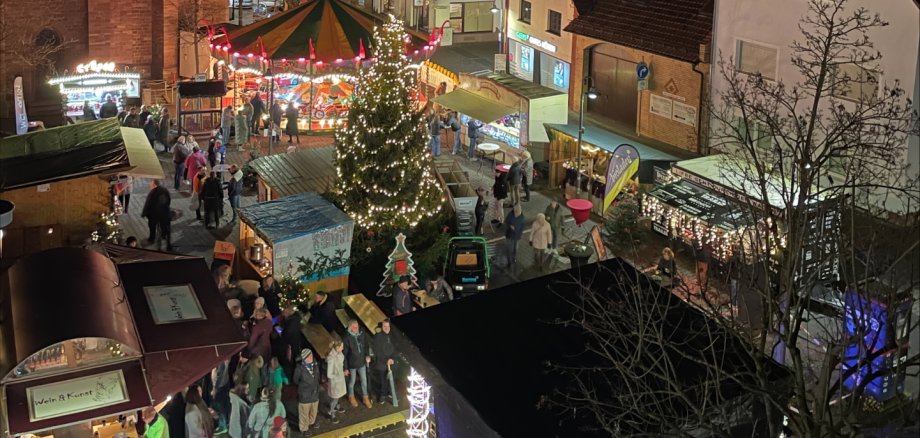Mercatino di Natale a Jügesheim Mercatino serale dell'Avvento nella piazza del municipio di Rodgau con albero di Natale illuminato, giostra e bancarelle di fronte agli edifici storici.