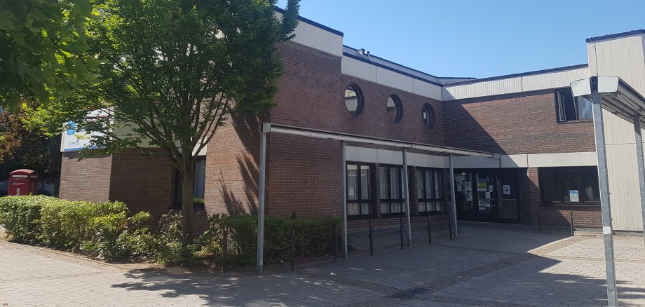 Wejście do centrum socjalnego Niederroden z ceglaną fasadą, kilkoma okrągłymi oknami i drzewami na pierwszym planie.