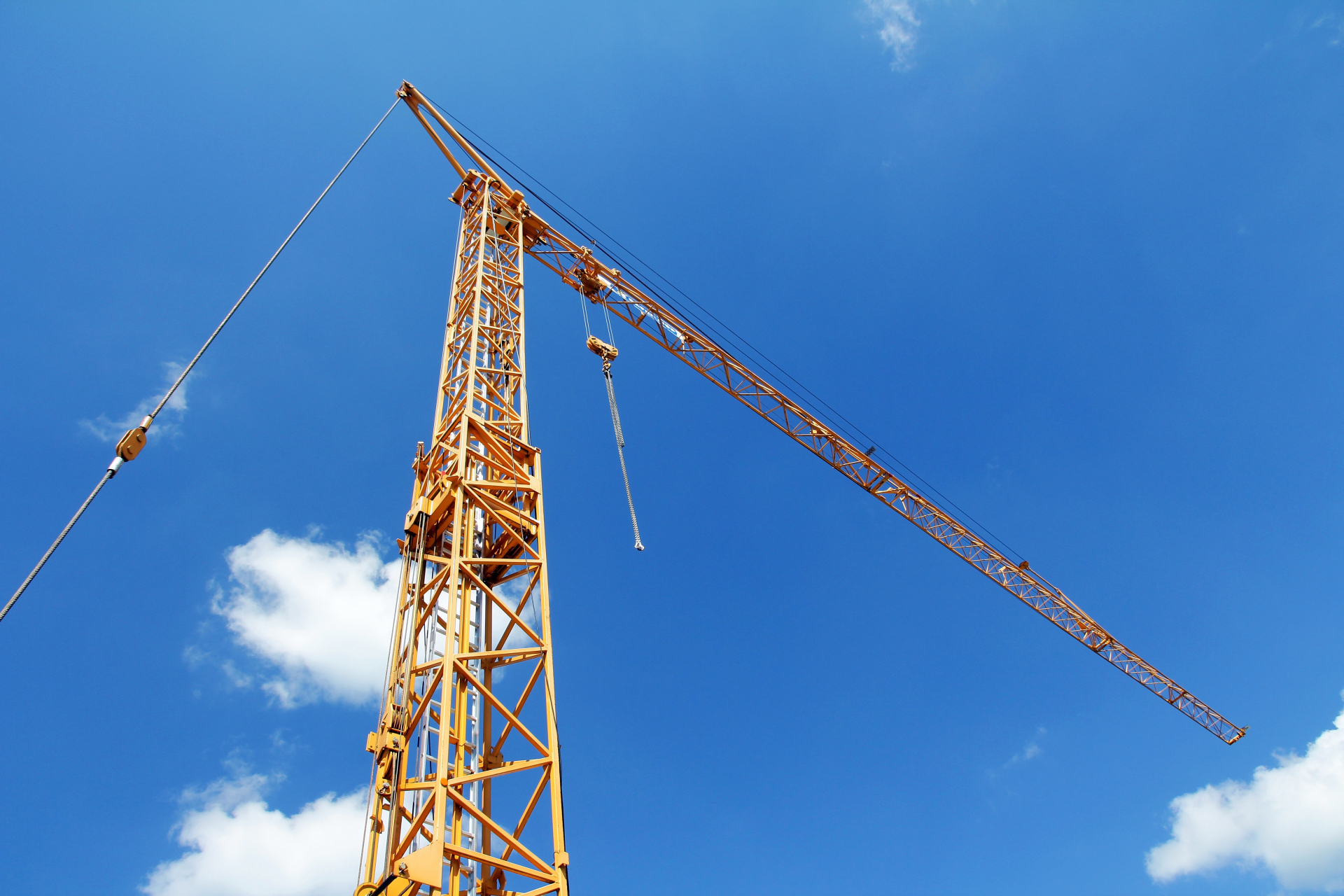Grua de construção amarela alta em frente a um céu azul com algumas nuvens brancas