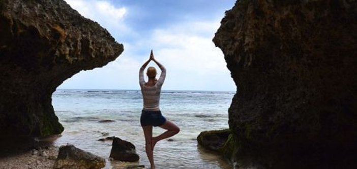 Yoga da vhs para o pescoço, os ombros e as costas Na prática de «yoga na árvore», a pessoa está em cima de uma rocha na praia, entre duas grandes rochas, com vista para o mar