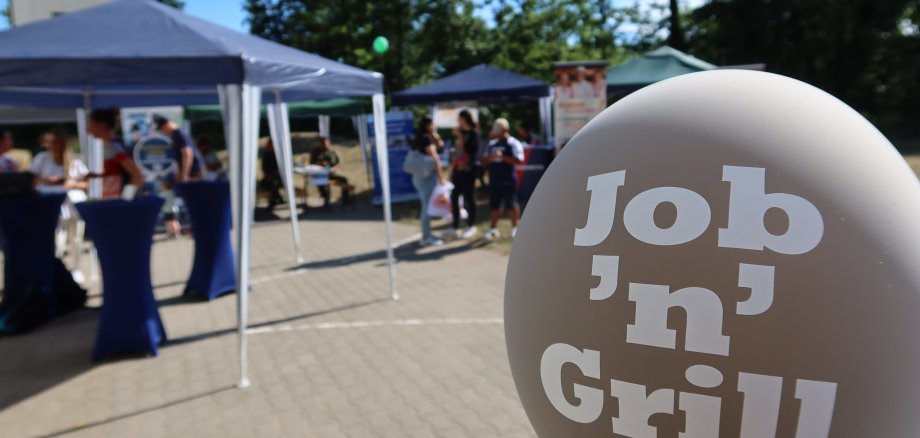 Balão com a etiqueta "Job 'n' Grill" em frente aos stands e visitantes de uma feira de educação ao ar livre