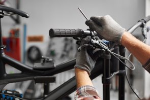 Reparação de uma bicicleta Um homem com luvas está a ajustar os travões do guiador de uma bicicleta com uma ferramenta.