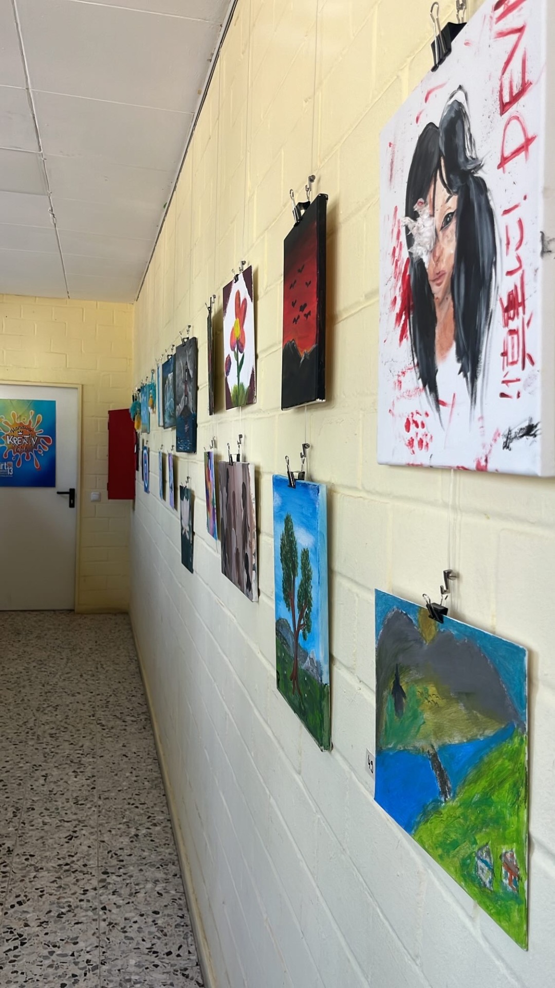 Obras de arte da JugendArt penduradas numa parede branca de um corredor, incluindo um retrato de uma mulher com cabelo preto e um fundo vermelho