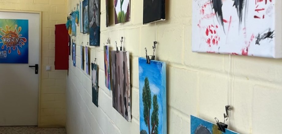 Obras de arte da JugendArt penduradas numa parede branca de um corredor, incluindo um retrato de uma mulher com cabelo preto e um fundo vermelho