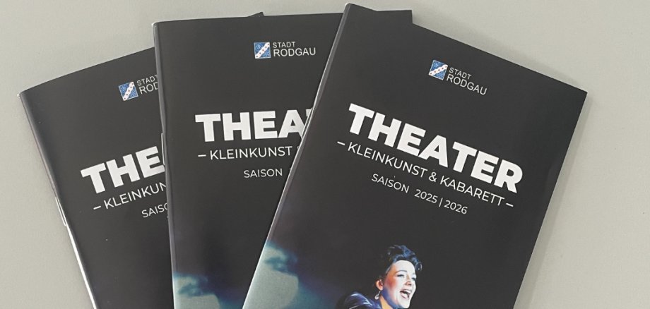 Trei broșuri de teatru de culoare neagră cu titlul "THEATER - KLEINKUNST & KABARET" pentru stagiunea 2025/2026, reprezentând o persoană în costum alb.