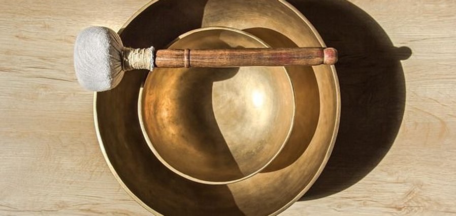 Ceremonia cu boluri tibetane Două boluri tibetane așezate unul în celălalt, cu un ciocănel așezat pe bolul de sus, pe o masă din lemn deschis la culoare