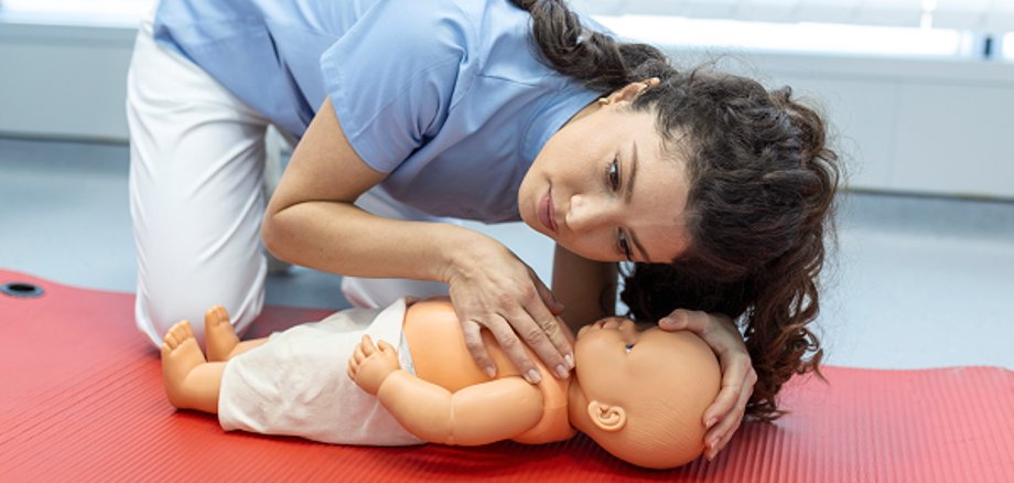 O persoană efectuează resuscitarea gură la gură a unei păpuși pe un covor roșu în cadrul unui curs de prim ajutor